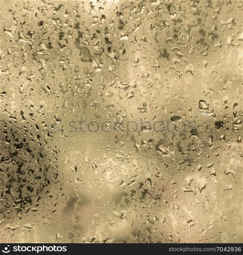 wet drops of water against glass pane with warm colored background