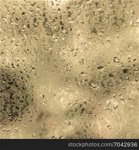 wet drops of water against glass pane with warm colored background