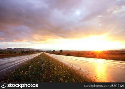 Wet road after rain and sunset over fields