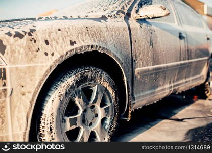 Wet vehicle in foam, automobile in suds, car wash. Carwash station. Wet vehicle in foam, automobile in suds, car wash