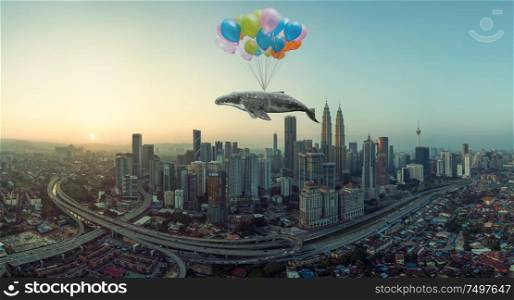 Whale floats in the air above the clouds with bunch of colorful balloons .
