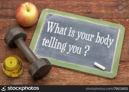 What is your body telling you? A question on a slate blackboard against weathered red painted barn wood with a dumbbell, apple and tape measure