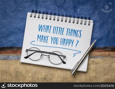 What little things make you happy? Inspiration question handwritten in a spiral notebook against colorful abstract paper landscape, happiness and personal development concept.
