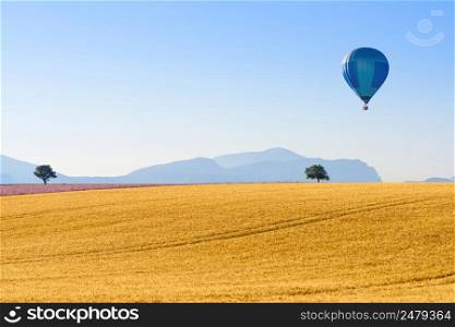 Wheat field curvy hill landscape with mountains and hot air balloon on horizon Provence France