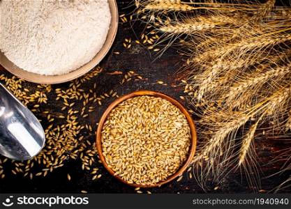 Wheat flour and wheat grains a bowl on the table. On a dark background. . Wheat flour and wheat grains a bowl on the table.