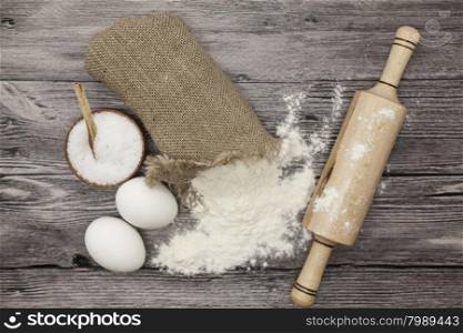 Wheat flour in a canvas bag, a large salt shaker wood, raw eggs, a wooden rolling pin: set for making homemade bread dough on a beautiful dark wooden background.