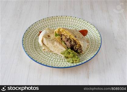 Wheat tortilla burrito stuffed with chipotle chicken, guacamole and rice with sauces on decorated plate