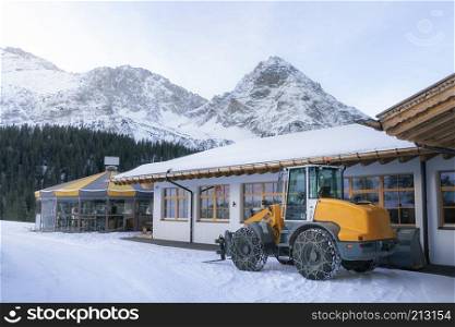 Wheel loader with chains on its tires, for plowing snow, in winter alpine scenery, the snow-capped Alps, a ski resort, in Ehrwald, Austria.