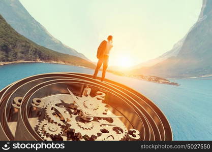 When time is passing. Businessman standing on old clock mechanism against sky background