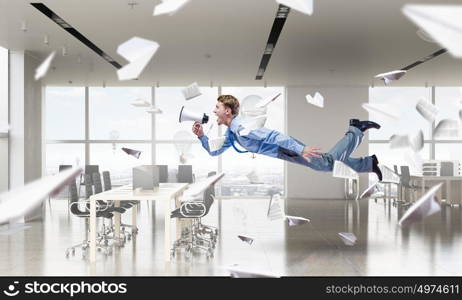 When tired of monotonous work. Young businessman flying in modern office interior and scream in megaphone