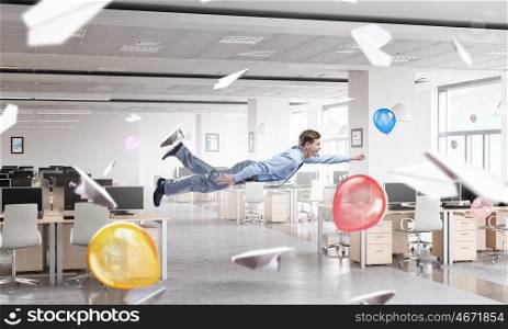 When tired of monotonous work. Young careless businessman flying in modern office interior