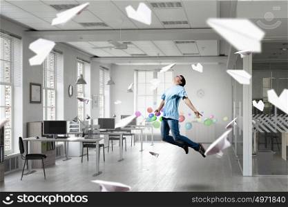 When tired of monotonous work. Young careless man flying in modern office interior