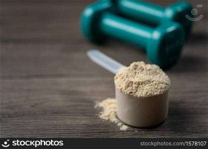 Whey protein powder in scoop and dumbbells. Sports drink, nutrition for muscle growth.