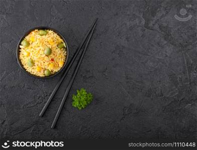 Whi Black bowl with boiled organic basmati vegetable rice with black chopsticks on black background. Yellow corn and green peas with paprika slices.