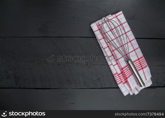 Whisk and tea towel on black wooden background.. Whisk and tea towel on black wooden background