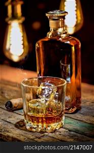 Whiskey in bottle and glass with cigar on wooden table. Glass of whiskey and cigar