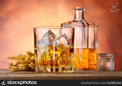 Whiskey with ice and ears of wheat on orange background