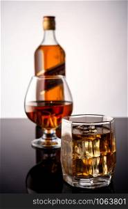 Whiskey with ice on a dark background. In the background a glass of whiskey and a full bottle of whiskey