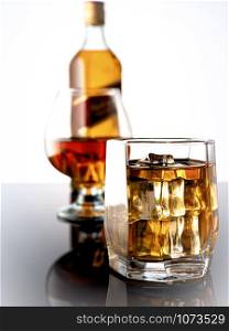 Whiskey with ice on a dark background. In the background a glass of whiskey and a full bottle of whiskey. Glass of whiskey with ice on a dark background. In the background a glass with whiskey and a bottle of whiskey