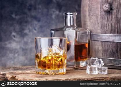 Whisky in glass and ice on the background of wooden barrels. Whisky in glass and ice