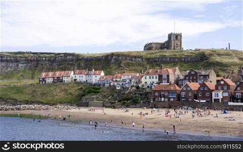Whitby, North Yorkshire, England - Aug 24, 2019:,UK.The harbour at Whitby on Yorkshire coast,View of people bathing in the sun, swimming and playing on the beach,Tourists on the sand beach in summer