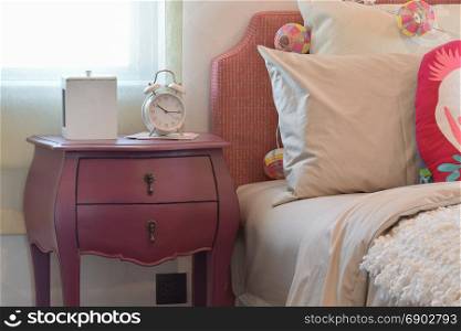 white alarm clock on bedside table and colorful pillows in modern kid bedroom interior
