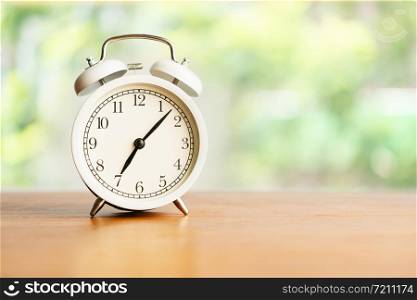 White alarm clock on brown wood desk on blurred background with copy space