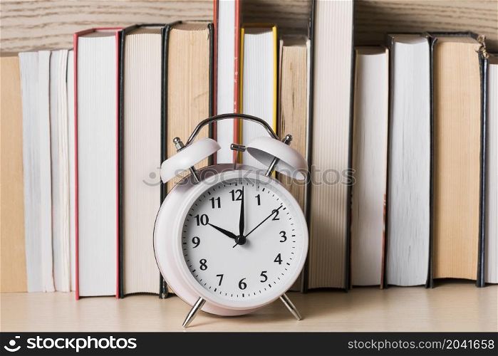 white alarm clock showing 10 o clock front bookshelf wooden desk