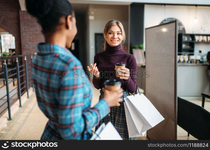 White and black females with shopping bags in mall. Shopaholics in clothing store, purchasing, fashion