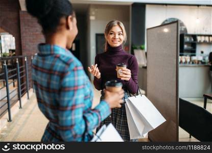 White and black females with shopping bags in mall. Shopaholics in clothing store, purchasing, fashion