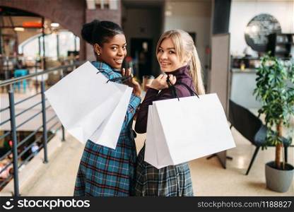 White and black lady with shopping bags in mall. Shopaholics in clothing store, purchasing, female buyers in shop