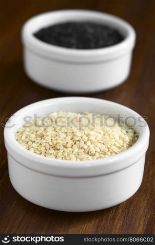 White and black sesame seeds in small bowls, photographed with natural light (Selective Focus, Focus one third into the white seeds)