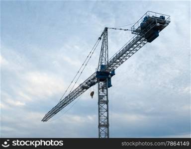 White and blue construction crane facing left against overcast gray sky.