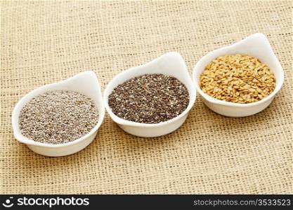 white and brown chia and golden flax seed in white ceramic bowls against burlap canvas