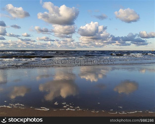 White and fluffy clouds over the wavy Baltic see with the beautiful reflections in the still water by the coastline