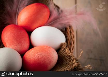 White and orange easter eggs on a light wooden background. Basket with colored easter eggs and feathers on a wooden background. Rustic style, place for your text.. White and orange easter eggs on a light wooden background.