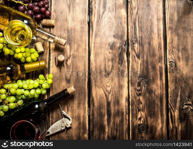 White and red wine with branches of grapes , a corkscrew and corks. On a wooden table.. White and red wine