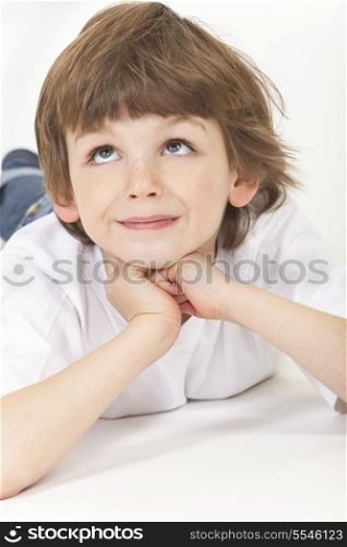White background studio photograph of young happy boy child laying down, resting on hands, looking up and thinking