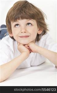 White background studio photograph of young happy boy child laying down, resting on hands, looking up and thinking