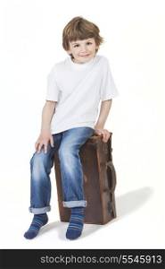 White background studio photograph of young happy boy smiling and sitting on a suitcase ready for vacation traveling