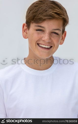 White background studio portrait of a smiling happy boy teenager teen male child with perfect teeth wearing a white t-shirt