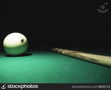 White ball number 8 from russian billiard pyramid and a cue on a table. Black background
