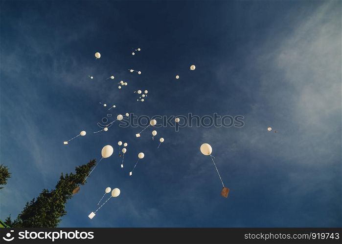White balloons fly up into the blue sky. The release of festive balloons in the clouds. Celebration and happiness. Air gel balls in the atmosphere.