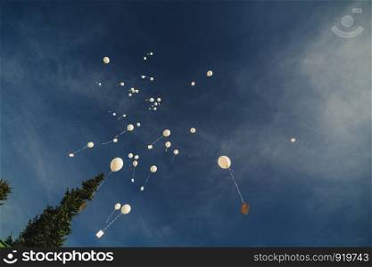 White balloons fly up into the blue sky. The release of festive balloons in the clouds. Celebration and happiness. Air gel balls in the atmosphere.
