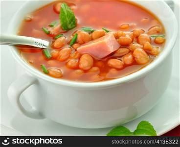 white bean soup with ham and tomatoes in a white soup cup