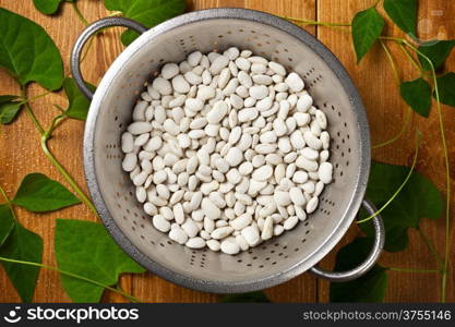 White beans with green leaves and water drops on wooden table. Top view shot
