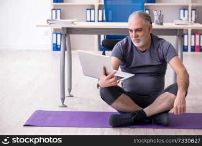 White bearded old man employee doing exercises in the office 