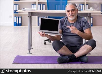 White bearded old man employee doing exercises in the office 