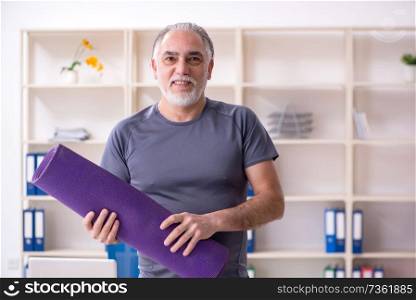 White bearded old man employee doing exercises in the office