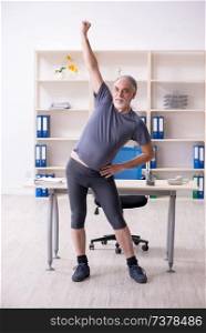 White bearded old man employee doing exercises in the office 